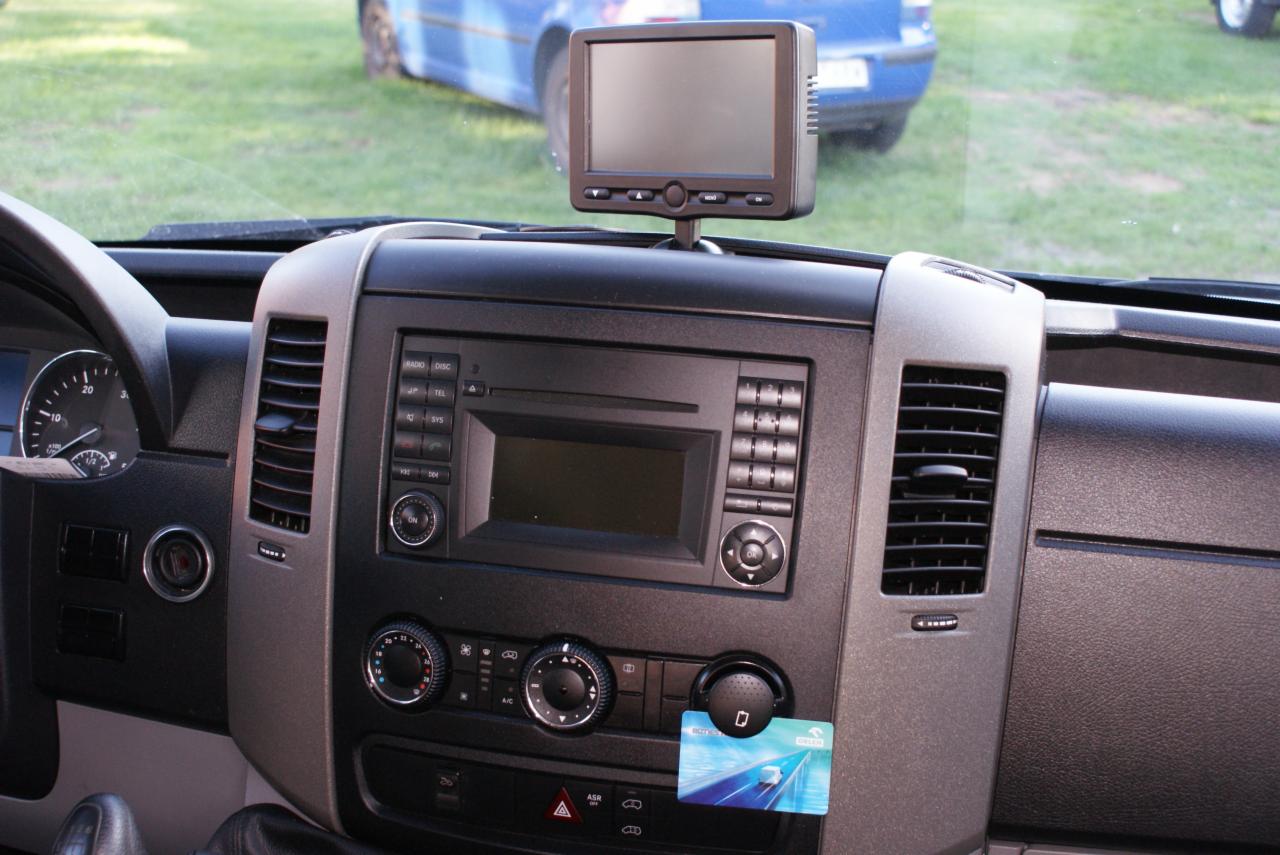 Wnętrze kabiny busa z systemem nawigacji i kartą paliwową Orlen, widok na deskę rozdzielczą i przednią szybę z fragmentem niebieskiego auta w tle.