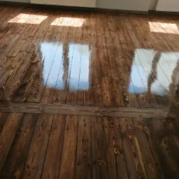 Błyszcząca, świeżo polakierowana podłoga z ciemnego drewna, odbijająca światło słoneczne z okien.