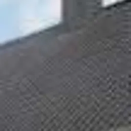 Szary dach z dachówki ceramicznej, widoczny komin z cegły, fragment nieba. Dach po renowacji, czysty i zadbany, z wyraźną fakturą dachówek.