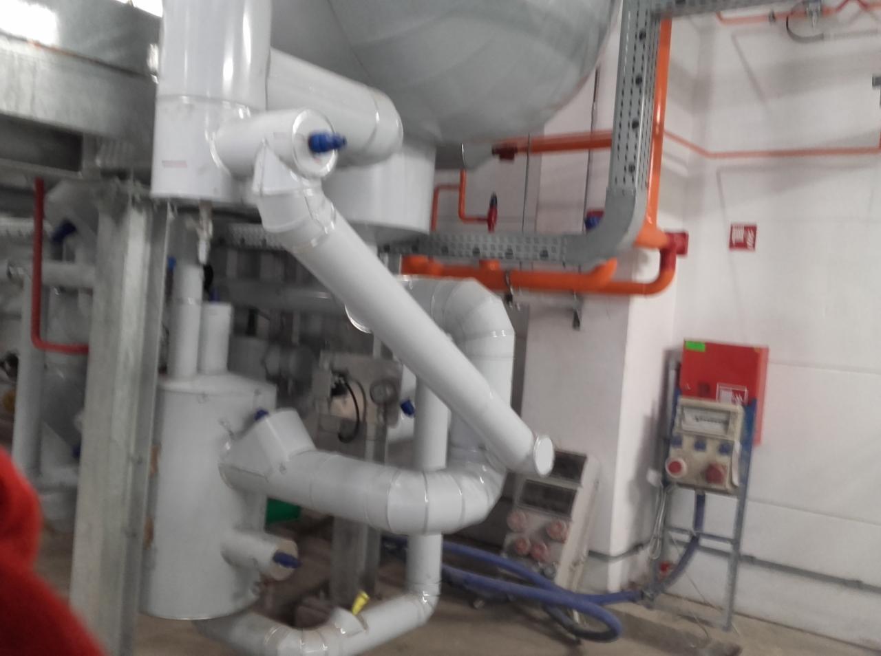 Instalacja przemysłowa z rurami, zbiornikami i panelami kontrolnymi, widoczne elementy połączeń i izolacji.