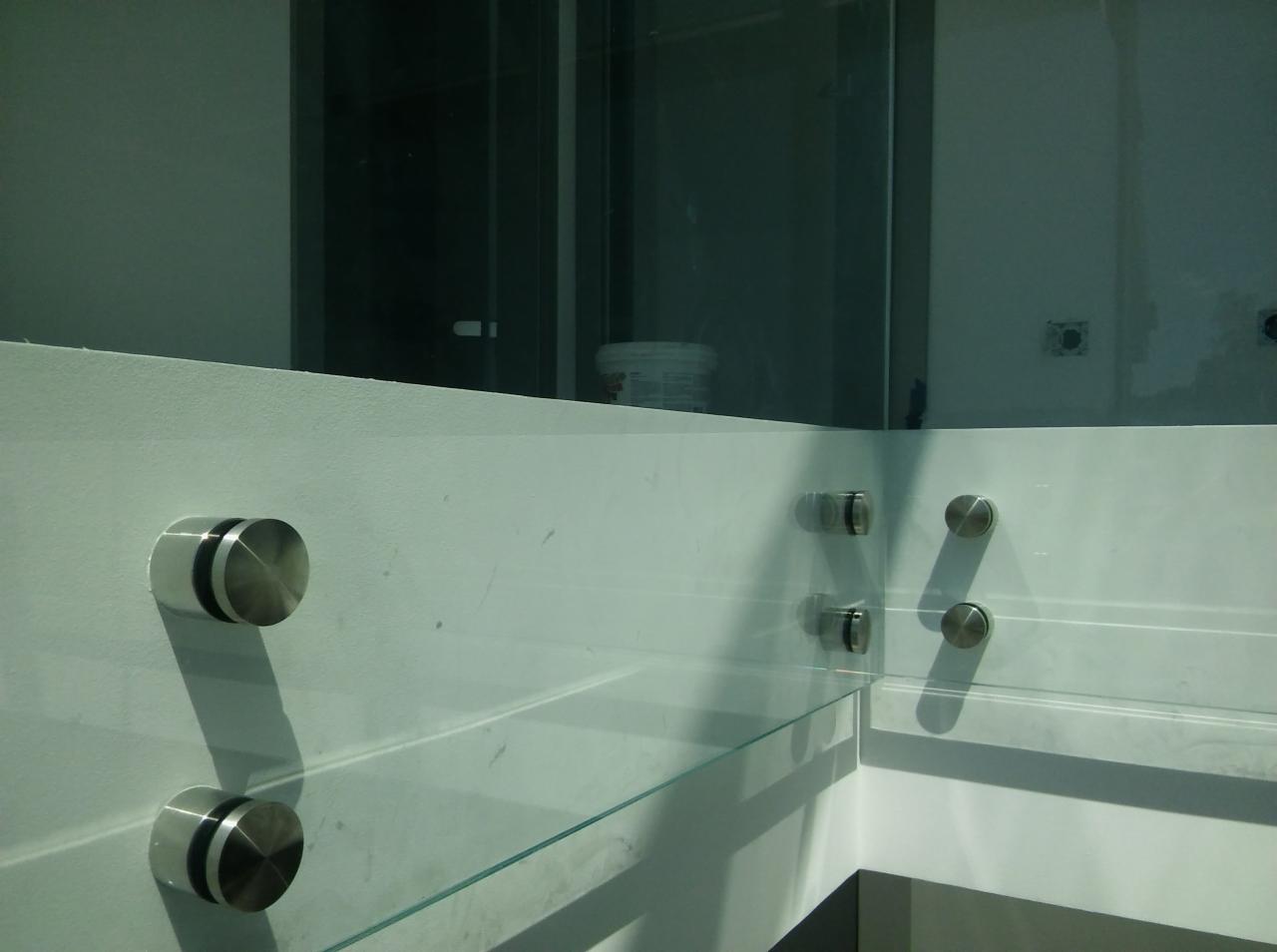 Całoszklana antresola zamocowana na rotulach w narożniku pomieszczenia, widoczne ślady po remoncie na ścianie.