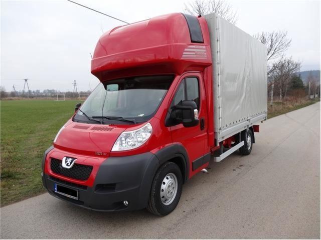 Czerwony bus dostawczy Peugeot z plandeką na pace, zaparkowany na drodze, widok z przodu. Typowy pojazd do przeprowadzek i transportu towarów.