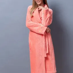 Kobieta w długim, koralowym szlafroku frotte z kolorowymi kropkami na mankietach, pozująca na szarym tle.