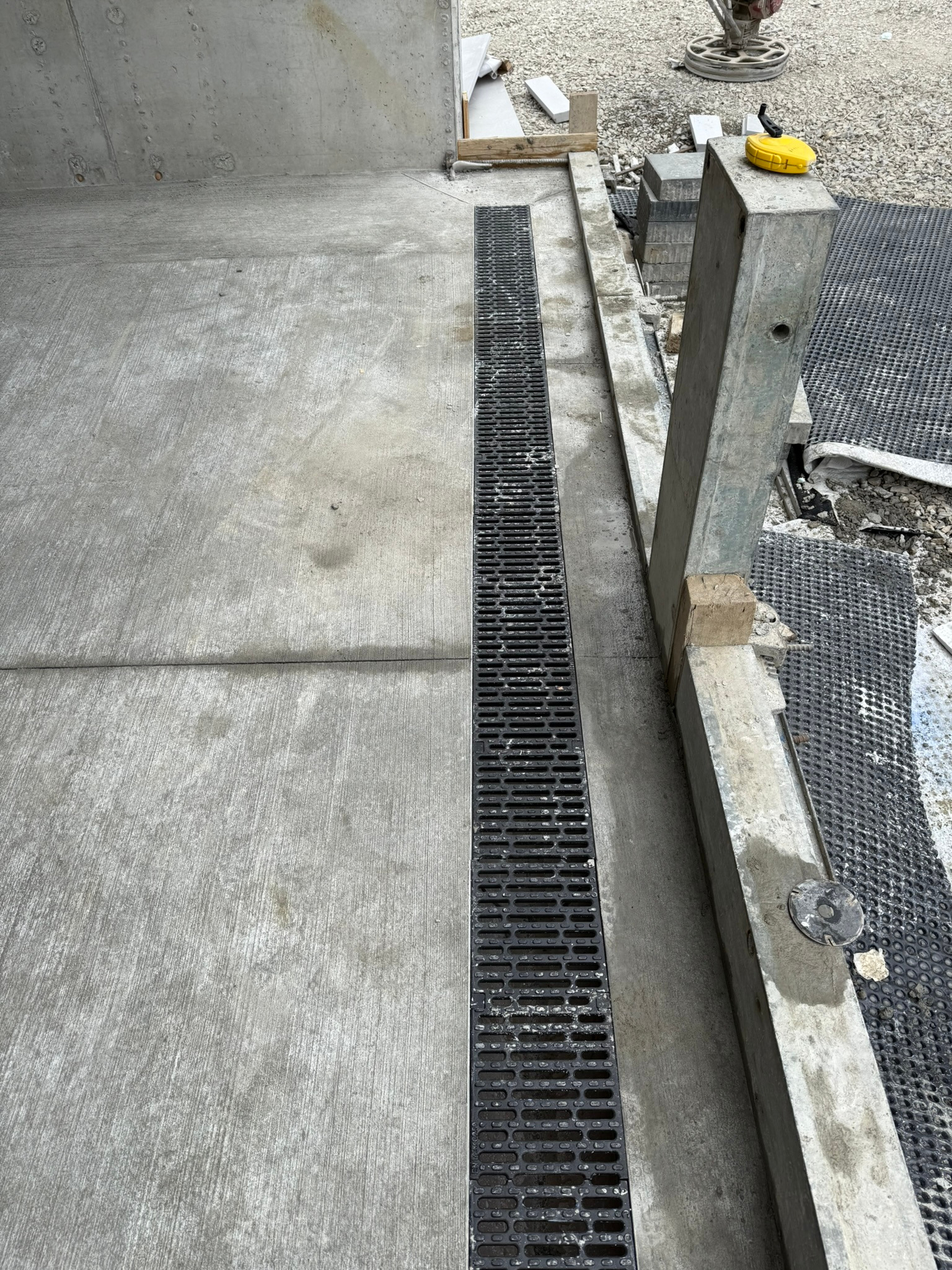 Szara, betonowa posadzka przemysłowa z czarnym odpływem liniowym. Widoczne elementy konstrukcyjne i narzędzia. Realizacja hali produkcyjnej.