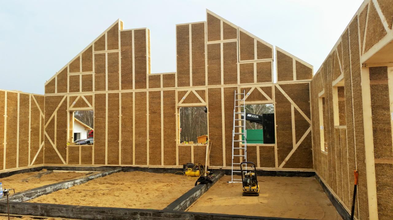 Konstrukcja domu modułowego w trakcie budowy: ściany wypełnione słomą, drewniane ramy, widoczne fundamenty i narzędzia budowlane. Dom w surowym stanie.