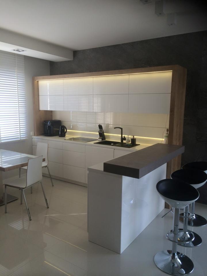 Biała, nowoczesna kuchnia na wymiar z wyspą i hokerami, oświetleniem LED podszafkowym i stołem z krzesłami. Realizacja w Toruniu.