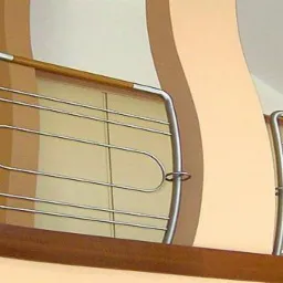 Nowoczesna balustrada schodowa ze stali nierdzewnej z drewnianym poręczą, z widocznym fragmentem rośliny doniczkowej i dekoracyjną kolumną w tle.