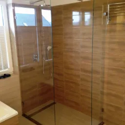 Nowoczesna kabina prysznicowa ze szklanymi ścianami i brązowymi płytkami, widoczny deszczownica, bateria i suszarka na ręczniki.