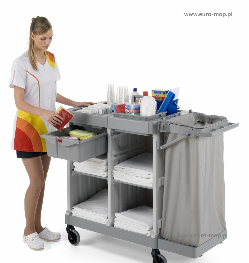 Wózek do sprzątania z wyposażeniem, obsługiwany przez kobietę w uniformie, przygotowany do serwisu hotelowego, z widocznymi ręcznikami i środkami czystości.