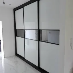 Nowoczesna szafa przesuwna z białymi i szarymi panelami, czarne ramy, biała marmurowa podłoga, widok z boku, surowe wykończenie pomieszczenia.