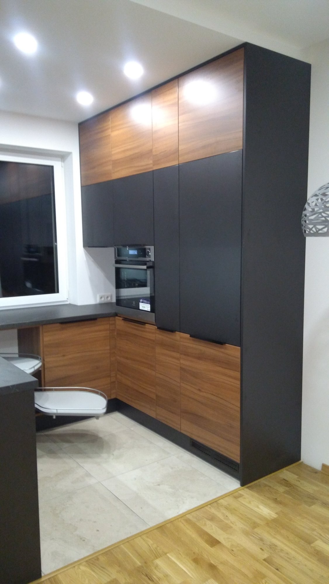 Nowoczesna kuchnia z frontami w kolorze drewna i antracytu, zabudowa sięgająca sufitu, piekarnik w zabudowie, narożna półka cargo.