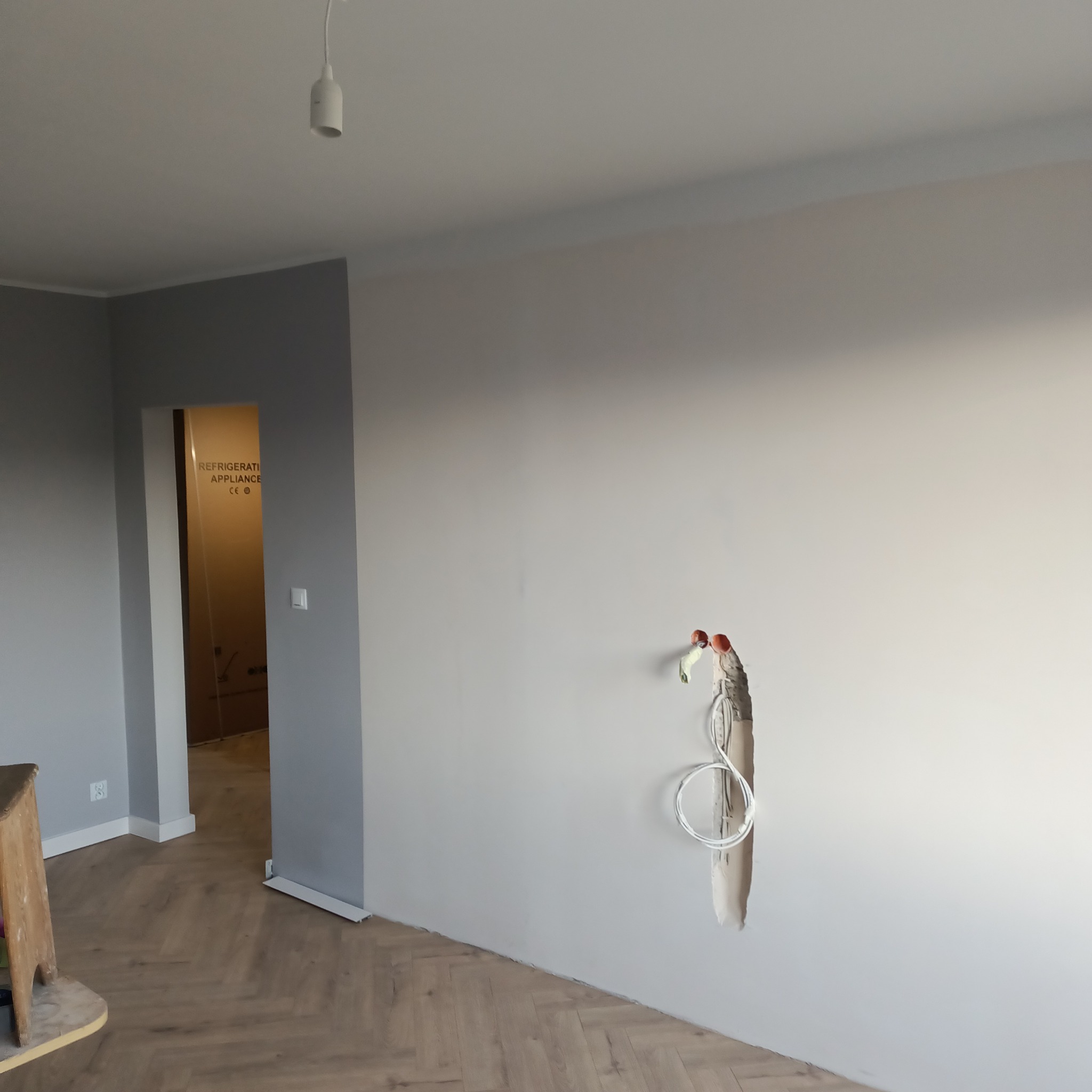 Szare ściany w nowym mieszkaniu z położoną podłogą w jodełkę, widoczne wystające kable ze ściany przed wykończeniem.