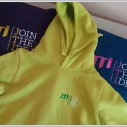 Jasnozielona bluza z kapturem z małym, wyhaftowanym logo firmy na piersi, obok granatowej i niebieskiej bluzy z większymi nadrukami logo tej samej firmy.