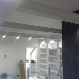 Nowoczesne oświetlenie sufitowe z reflektorami punktowymi i dekoracyjnym panelem ściennym w odcieniach szarości, widok na białe półki wnękowe.