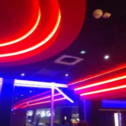 Nowoczesny sufit podwieszany z czerwonymi, okrągłymi elementami i niebieskimi liniami LED w ciemnym wnętrzu. Widoczny fragment wentylacji i czujnik dymu.