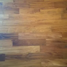 Ułożona podłoga z paneli drewnianych w ciepłych odcieniach brązu, z widocznym wzorem słojów. Ujęcie z góry, ukazujące detale faktury drewna i łączenia desek.