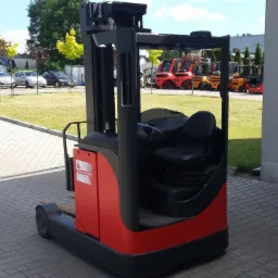 Czerwono-czarny wózek widłowy wysokiego składowania Linde R16, z widocznym siedzeniem operatora i elementami sterującymi, zaparkowany na kostce brukowej przed budynkiem, w tle inne wózki widłowe...