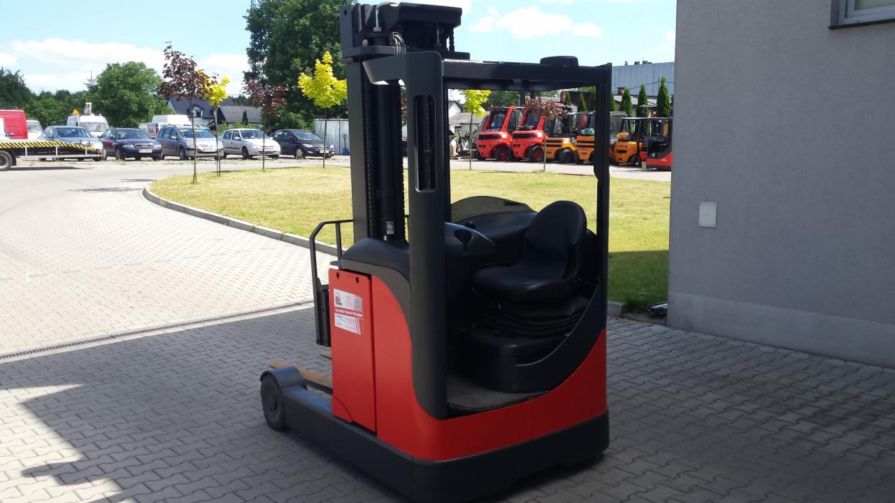 Czerwono-czarny wózek widłowy wysokiego składowania Linde R16, z widocznym siedzeniem operatora i elementami sterującymi, zaparkowany na kostce brukowej przed budynkiem, w tle inne wózki widłowe...