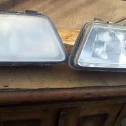 Porównanie dwóch reflektorów samochodowych: stary zmatowiały i nowy, przezroczysty, leżące na drewnianej powierzchni.