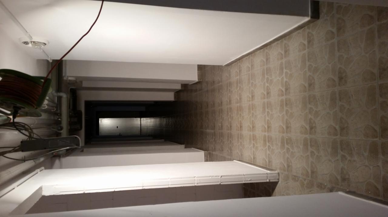 Wnętrze klatki schodowej z pomalowanymi schodami i ścianami wyłożonymi płytkami. Widoczna instalacja elektryczna i zwój kabla.