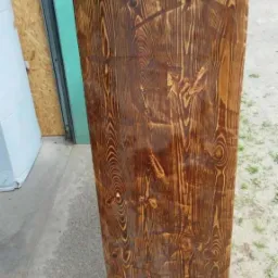 Lakierowana, brązowa kolumna z drewna ze sękami, z czterema ozdobnymi, wystającymi elementami na górze i dole. Widoczne pionowe usłojenie drewna.