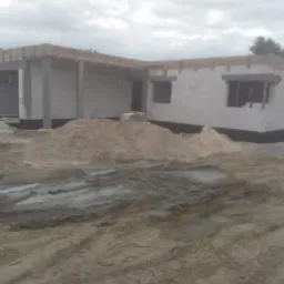 Stan surowy otwarty domu z garażem w trakcie budowy, widoczne szalunki i materiały budowlane na błotnistym terenie.