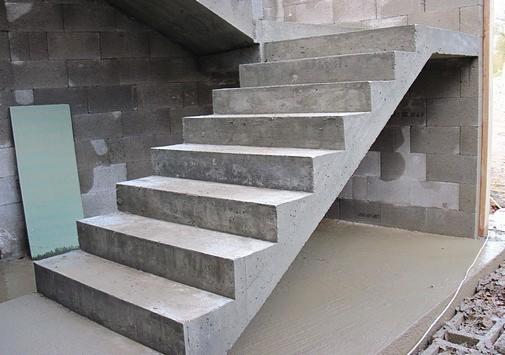 Surowe, betonowe schody w trakcie budowy, z widoczną ścianą z bloczków betonowych i zieloną płytą opartą o ścianę. Widoczne ślady zaprawy.
