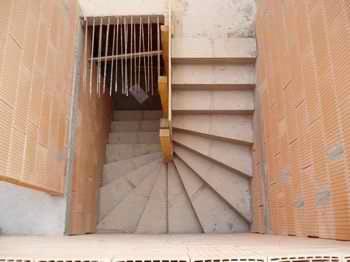 Spiralne schody z betonu surowego w trakcie montażu, widok z góry. Elementy drewniane poręczy. Ściany z cegieł ceramicznych.