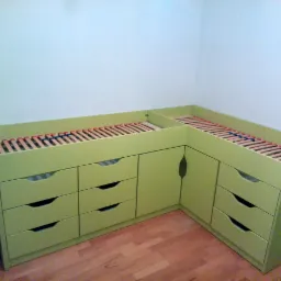 Zielone łóżko na antresoli z szafkami i szufladami w rogu pokoju, widoczne drewniane listwy pod materac.