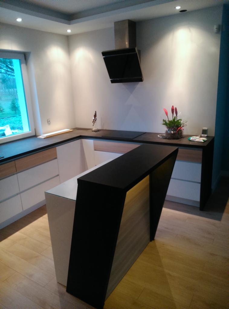 Nowoczesna kuchnia z wyspą w jasnych barwach we Wrocławiu, z czarnym blatem i oświetleniem punktowym, widok z niskiego kąta.