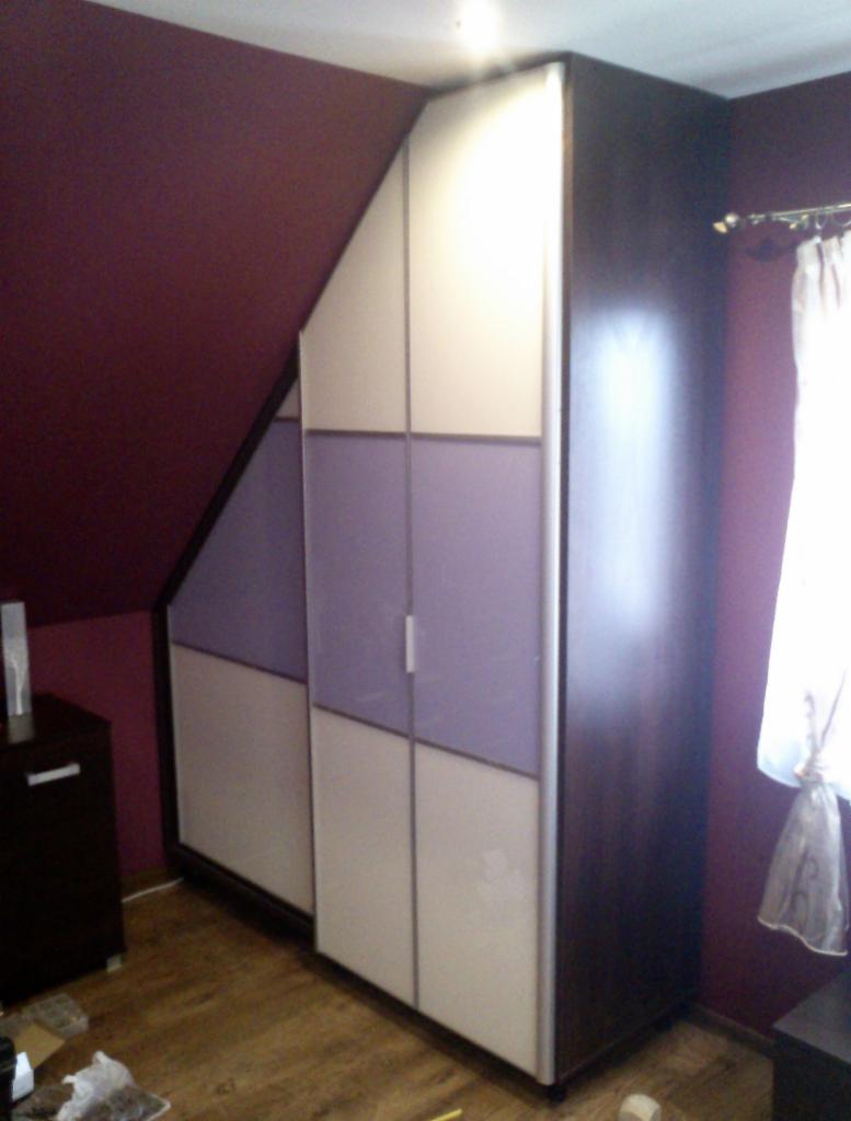 Szafa wnękowa na poddaszu z przesuwnymi drzwiami, łącząca panele białe i fioletowe, dopasowana do skosu dachu, z widocznym fragmentem podłogi i ściany w kolorze burgundowym.