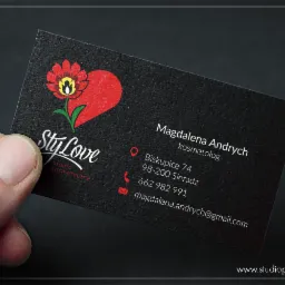 Czarna wizytówka studia kosmetycznego z logo w kształcie serca i kwiatka, trzymana w dłoni, prezentująca dane kontaktowe Magdaleny Andrych, kosmetologa.