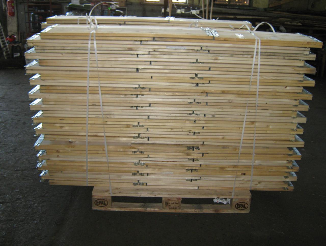Stos desek z metalowymi wzmocnieniami na palecie EPAL, spięty sznurkiem. Widoczne niedoskonałości drewna i faktura betonu na podłodze.