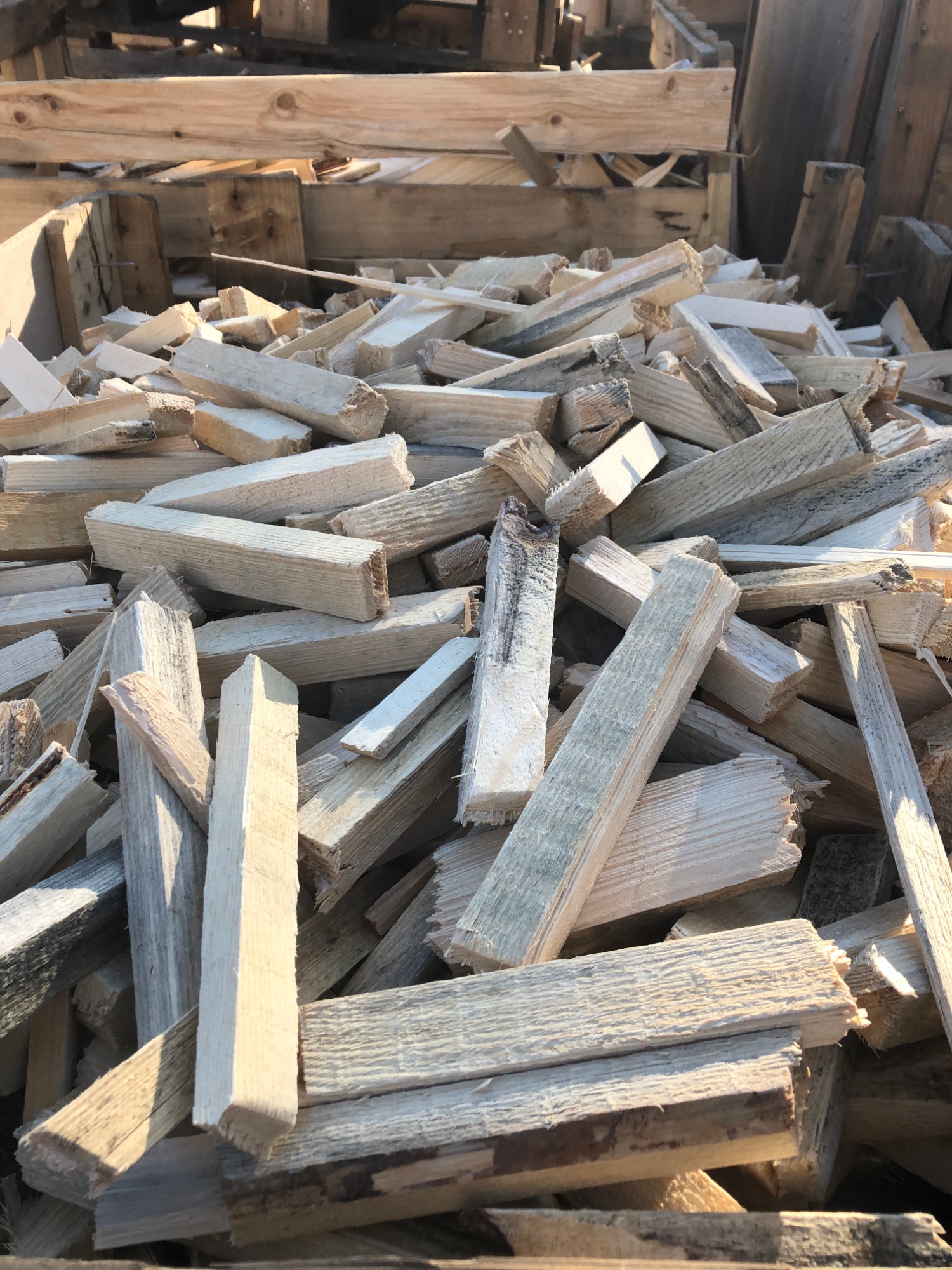 Stos pociętych kawałków drewna, prawdopodobnie odpadów produkcyjnych, o nieregularnych kształtach i fakturze, ułożonych na tle drewnianej konstrukcji.