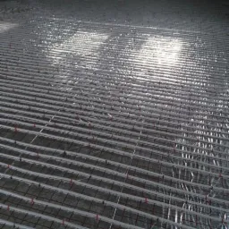 Przygotowana instalacja ogrzewania podłogowego z rurami, siatką i folią refleksyjną, widoczne czerwone mocowania, surowy stan ścian z cegieł.