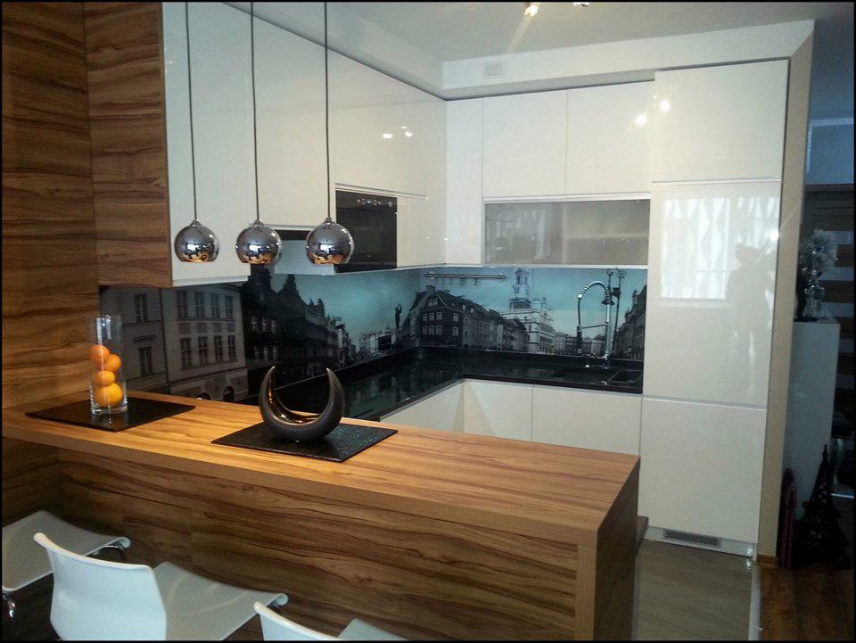 Nowoczesna kuchnia z białymi, lakierowanymi szafkami, drewnianym blatem i panelem ściennym z motywem miejskim, oświetlona trzema chromowanymi lampami wiszącymi.