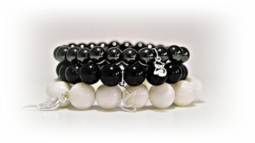 Trzy bransoletki z koralików: białe, czarne i ciemnoszare, z zawieszkami w kształcie piór i cyfry 23, na białym tle.