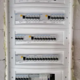 Rozdzielnica elektryczna z wieloma zabezpieczeniami różnicowoprądowymi i nadprądowymi marki Eaton i Tracon, zamontowana na ścianie w surowym stanie.