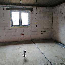 EL - KAB Usługi Elektryczne - Surowy stan wnętrza w Bliżynie, z widocznymi przewodami elektrycznymi wychodzącymi ze ściany, niezabudowanymi puszkami elektrycznymi i metalowymi profilami pod sufitem, wskazującymi na etap prac...