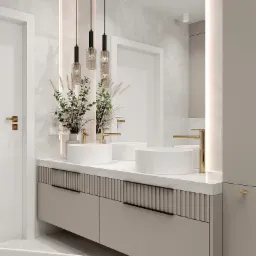 Elegancka łazienka z dwoma białymi umywalkami nablatowymi, złotymi bateriami i wiszącymi lampami z dekoracyjnego szkła, dopełniona kompozycją z wysokich traw i zieleni w ceramicznych wazonach.