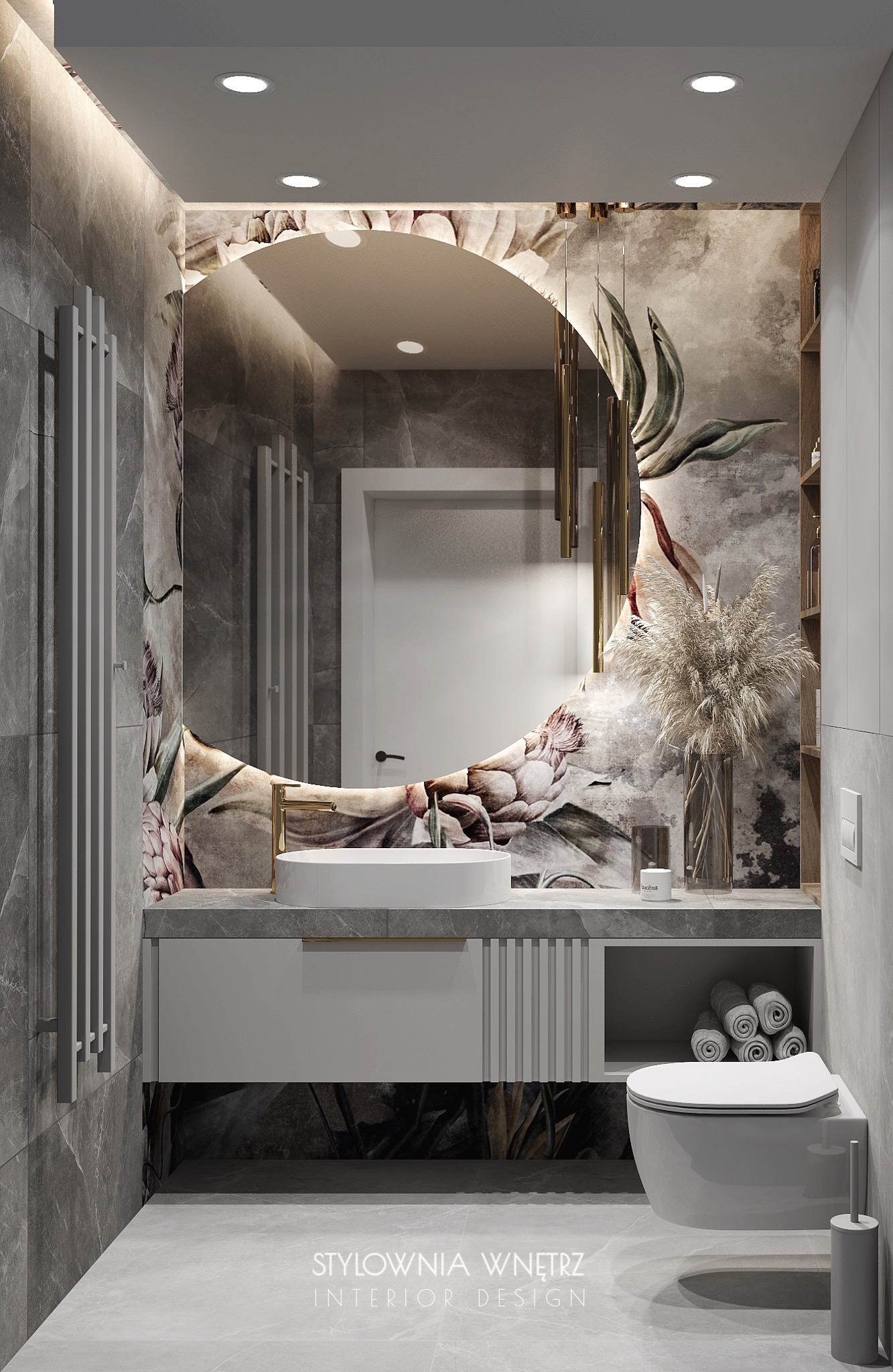 Elegancka łazienka w szarościach z motywem kwiatowym na ścianie, okrągłe lustro z podświetleniem, biała umywalka nablatowa z złotą baterią, wisząca toaleta i dekoracyjna trawa w wazonie.