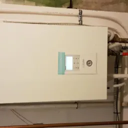 Zamontowana pompa ciepła Panasonic Aquarea z widocznymi rurami instalacji grzewczej i zaworami, zainstalowana na ścianie w pomieszczeniu technicznym.