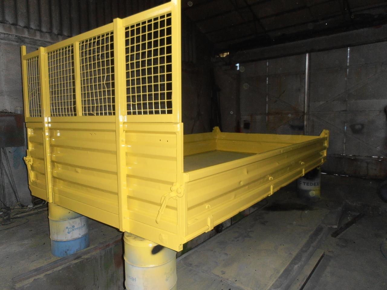 Żółta, odnowiona skrzynia ładunkowa samochodu dostawczego z metalową kratownicą, ustawiona na beczkach w warsztacie.