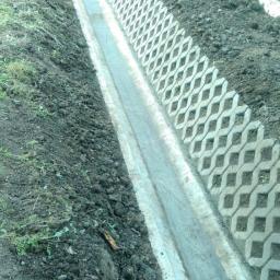 REMODOM SPÓŁKA Z OGRANICZONĄ ODPOWIEDZIALNOŚCIĄ - Długi, betonowy rów odwadniający wyłożony ażurowymi, betonowymi płytami wzdłuż ogrodzenia z siatki.