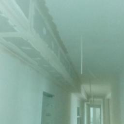 REMODOM SPÓŁKA Z OGRANICZONĄ ODPOWIEDZIALNOŚCIĄ - Korytarz w trakcie montażu płyt kartonowo-gipsowych na suficie, widoczne profile i częściowo położona gładź szpachlowa.