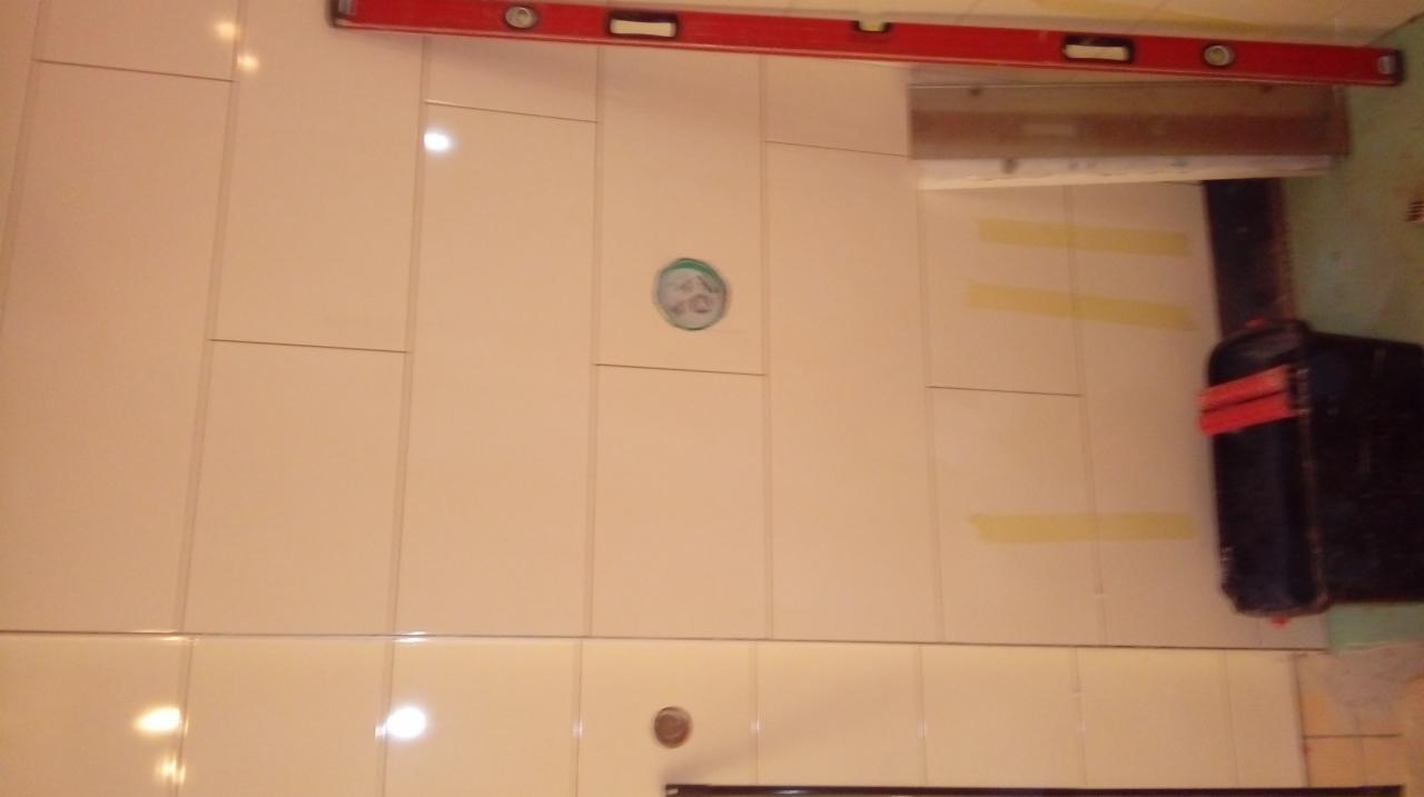 Świeżo położone, jasne płytki ścienne z widocznymi otworami na instalacje, poziomica i skrzynka narzędziowa w tle.