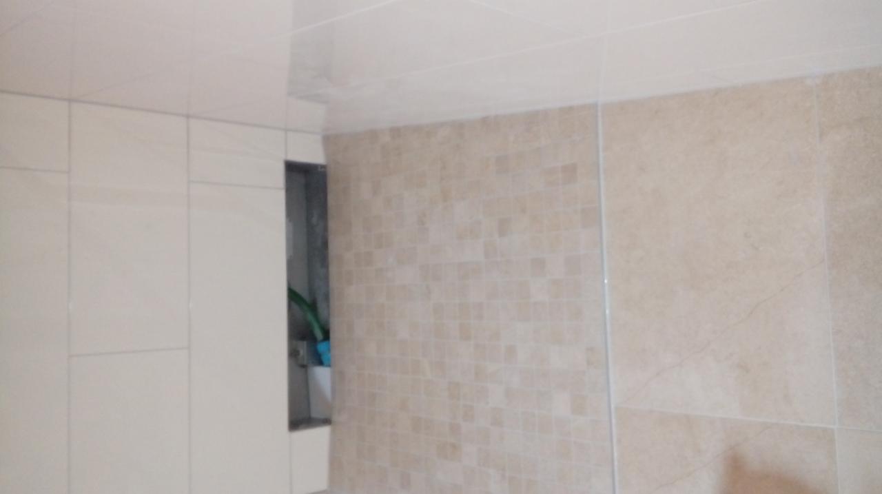 Beżowe płytki ceramiczne o różnych wzorach i rozmiarach na ścianie w łazience, widoczna wnęka z zielonym wężem odkurzacza.