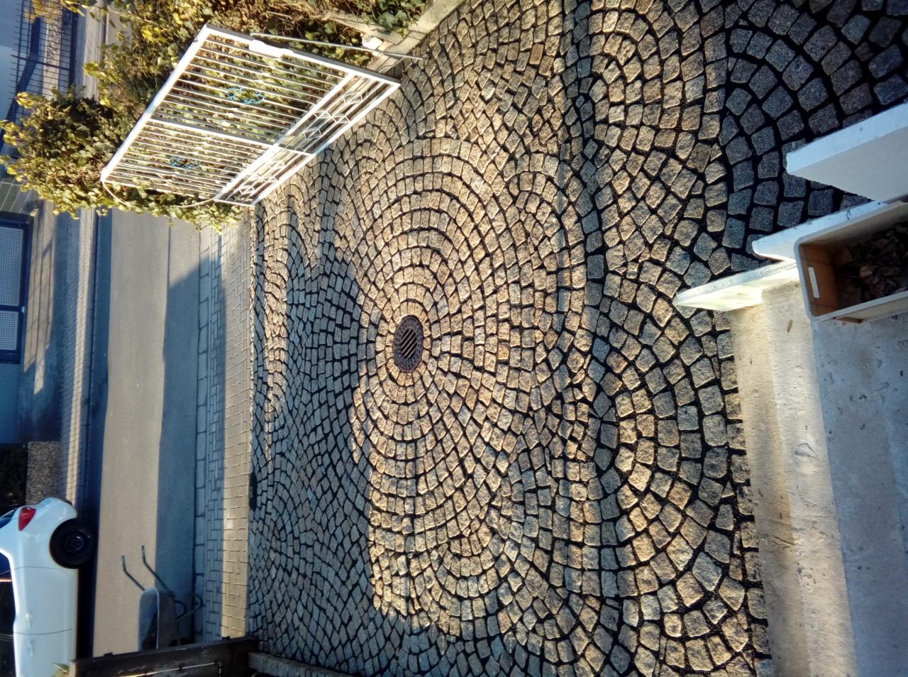 Ułożona z kostki brukowej nawierzchnia z centralnie umieszczonym odpływem, tworząca wzór koncentrycznych okręgów, oświetlona bocznym światłem słonecznym.