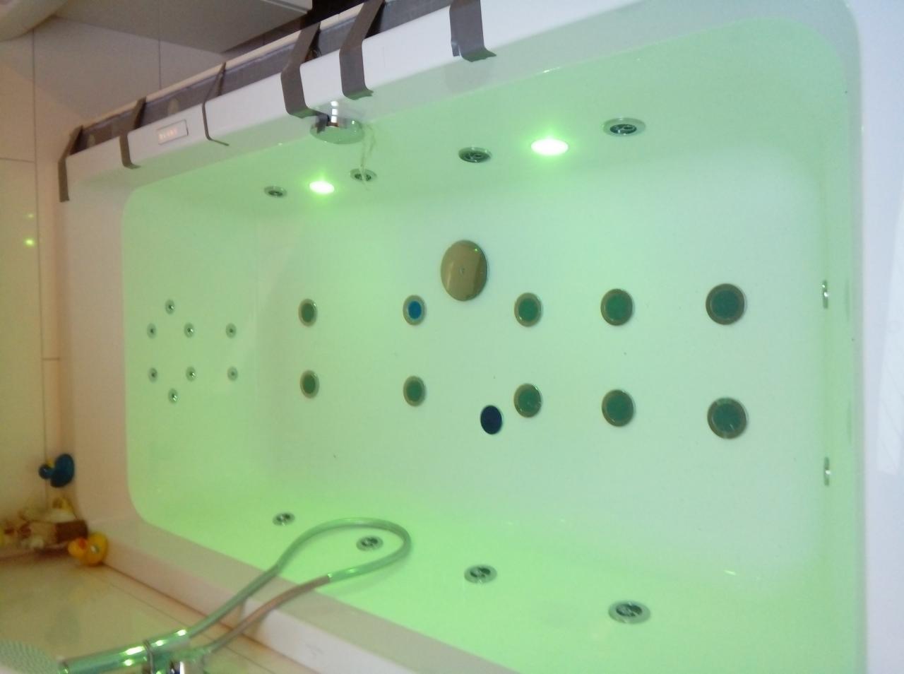 Nowoczesna wanna z hydromasażem wypełniona wodą, podświetlana zielonym światłem, z widocznymi dyszami i armaturą.