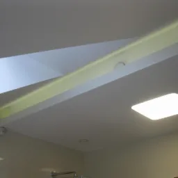 Nowoczesny sufit podwieszany z oświetleniem LED, widoczne detale wykończenia i elementy wentylacyjne. Jasne, minimalistyczne wnętrze z subtelnym oświetleniem.